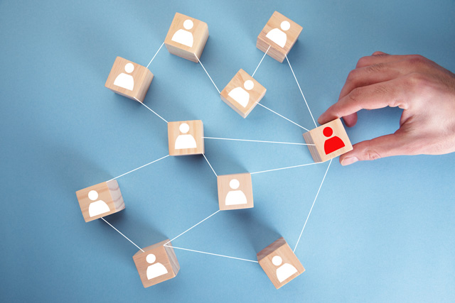 Auf mehreren Holzwürfeln ist eine Spielfigur abgebildet. Die Würfel sind mit Fäden miteinander verbunden. Eine Figur ist rot. Die anderen sind weiß. Das Bild steht für die Akteure hinter der digitalen Baugenehmigung